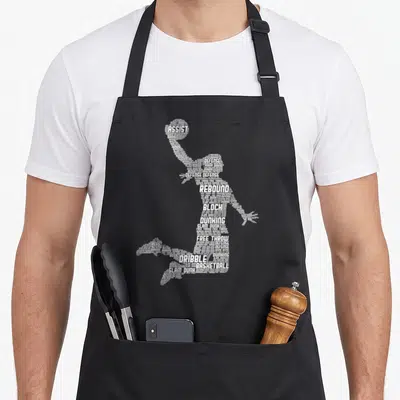 Cute basketball apron - White word art silhouette of a basketball player formed by terms like assist, defense, rebound — shown on a black cotton canvas apron against a white background