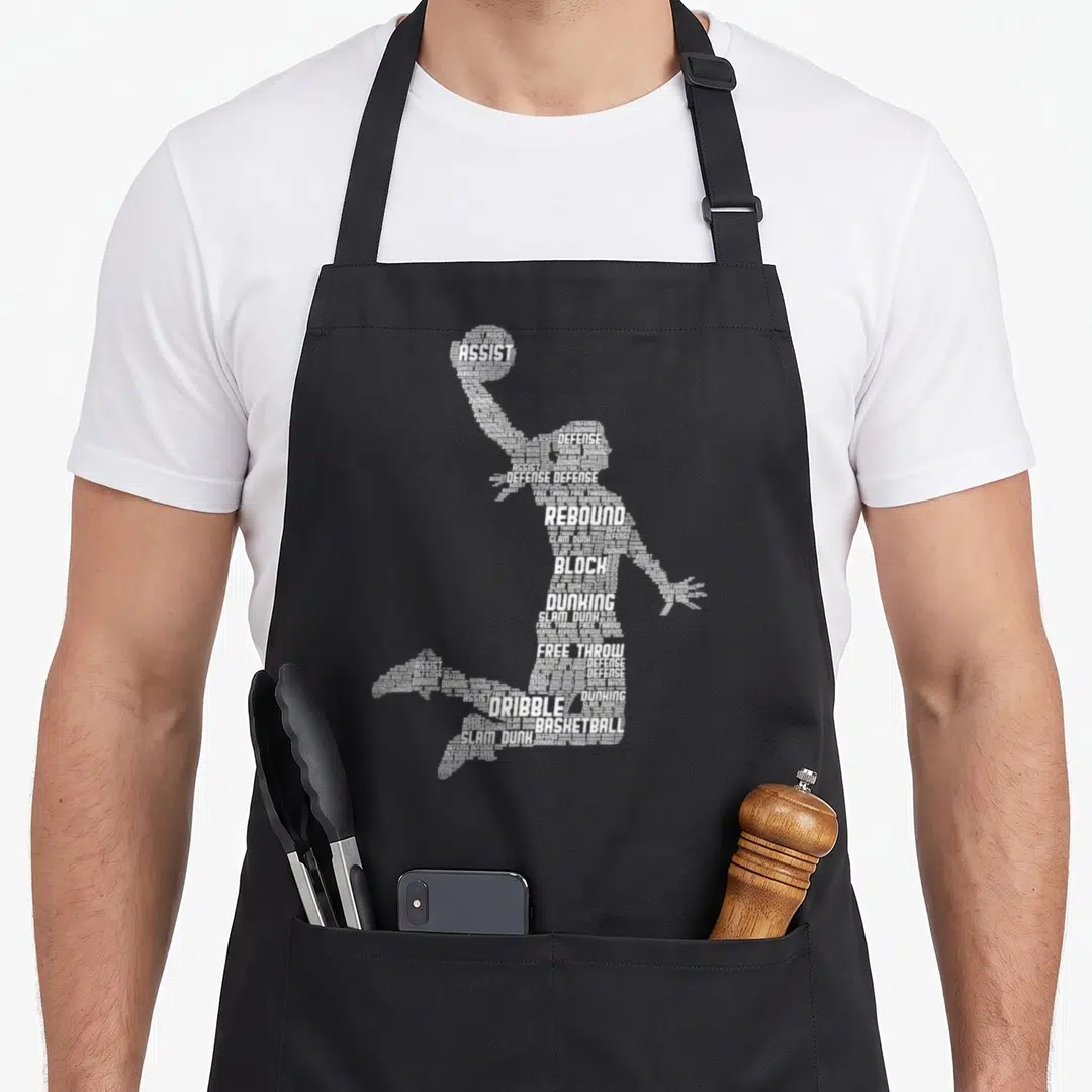 Cute basketball apron - White word art silhouette of a basketball player formed by terms like assist, defense, rebound — shown on a black cotton canvas apron against a white background