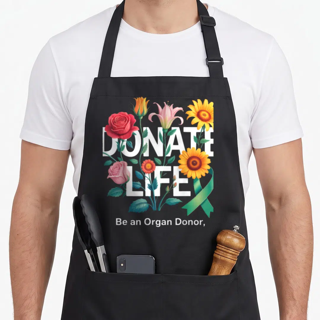 Floral organ apron - DONATE LIFE text with realistic roses, lilies, sunflowers, and a green ribbon — shown on a black cotton canvas apron against a white background