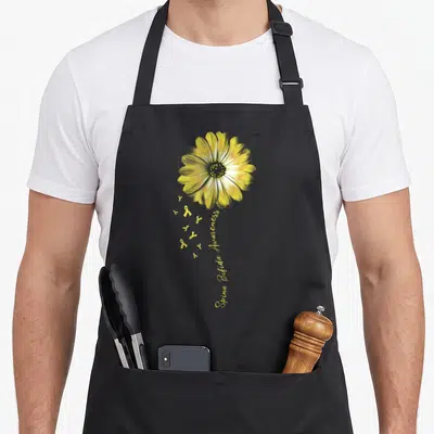 Spina daisy apron - Realistic yellow daisy with green accents and small ribbons forming a stem with text below — shown on a black cotton canvas apron against a white background