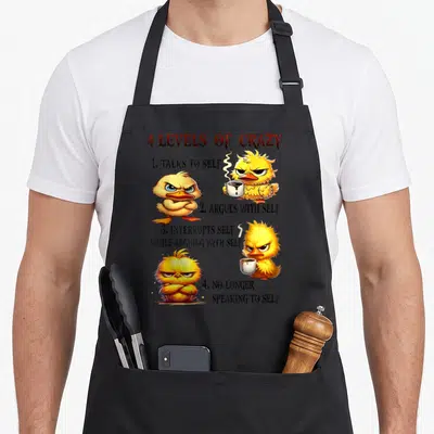 Level cotton duck aprons - Grumpy yellow ducklings holding coffee cups next to 4 Levels of Crazy text list — shown on a black cotton canvas apron against a white background