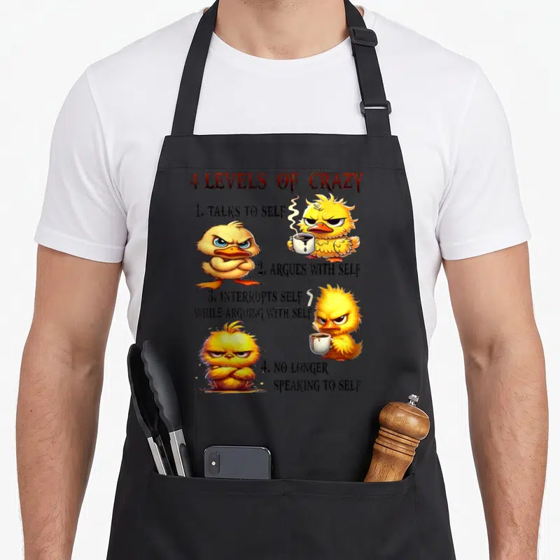 Level cotton duck aprons - Grumpy yellow ducklings holding coffee cups next to 4 Levels of Crazy text list — shown on a black cotton canvas apron against a white background