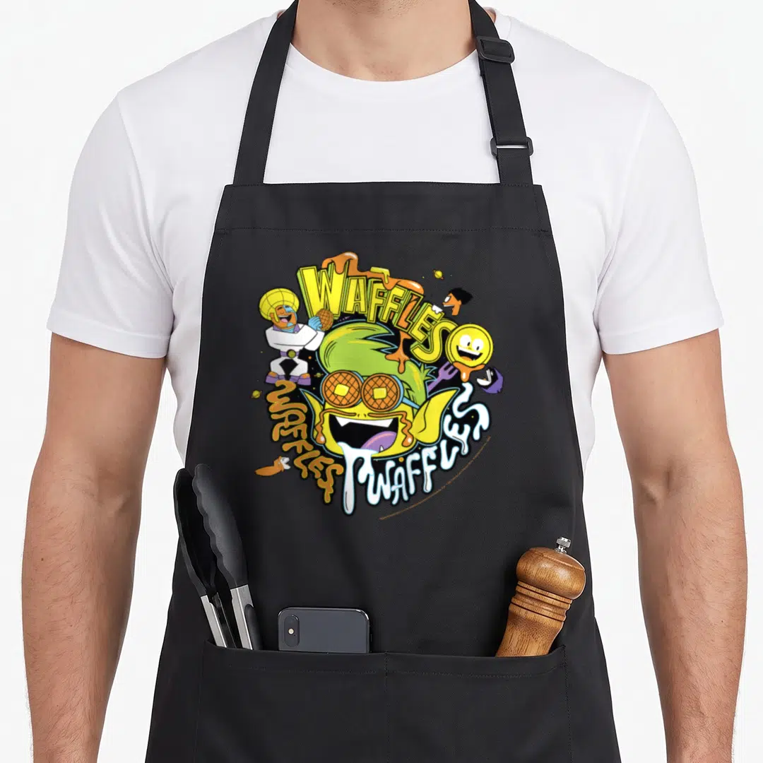 Beast 2t apron - Waffle monster with syrup and WAFFLES text in yellow, green, orange, and white cartoon style — shown on a black cotton canvas apron against a white background