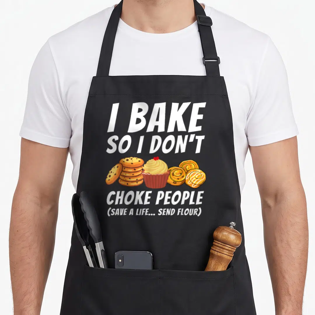 Choke baker apron - Cartoon cookies, cupcake, and cinnamon rolls under text I Bake So I Don't Choke People — shown on a black cotton canvas apron against a white background