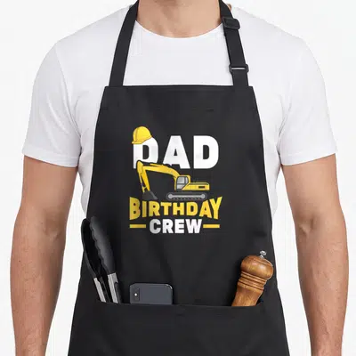 Digger construction apron - Yellow excavator and DAD BIRTHDAY CREW text with hard hat graphic — shown on a black cotton canvas apron against a white background