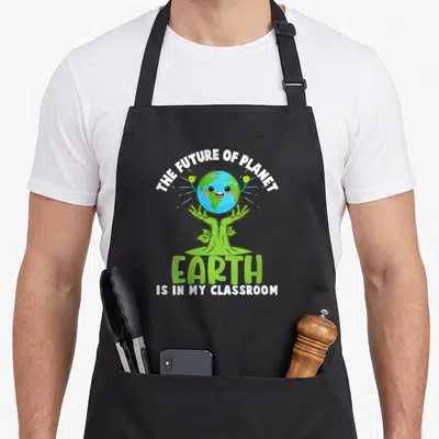 Earth future teacher apron - Cartoon Earth held by tree hands with text THE FUTURE OF PLANET EARTH IS IN MY CLASSROOM — shown on a black cotton canvas apron against a white background