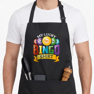 Lucky player bingo apron - Cartoon graphic of five colorful numbered bingo balls with MY LUCKY BINGO SHIRT text — shown on a black cotton canvas apron against a white background