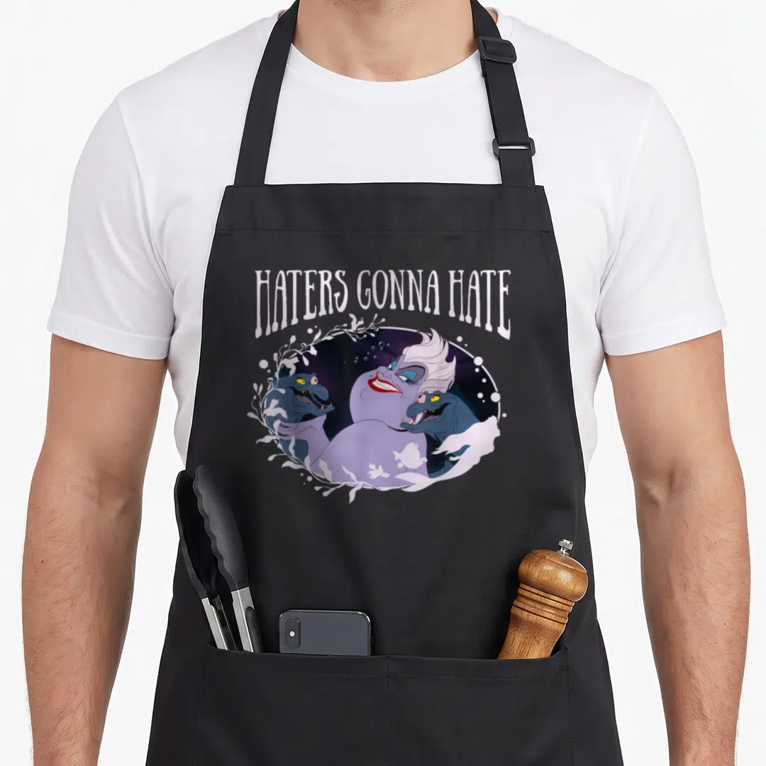 Ursula mermaid apron - Haters Gonna Hate text above Ursula and two eels in purple and blue — shown on a black cotton canvas apron against a white background