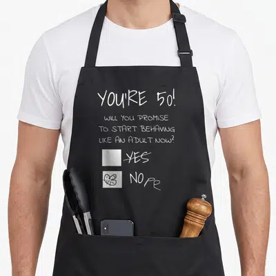 Present joke apron - White text asking about adult behavior with NOPE checkbox scribbled and YES crossed out — shown on a black cotton canvas apron against a white background