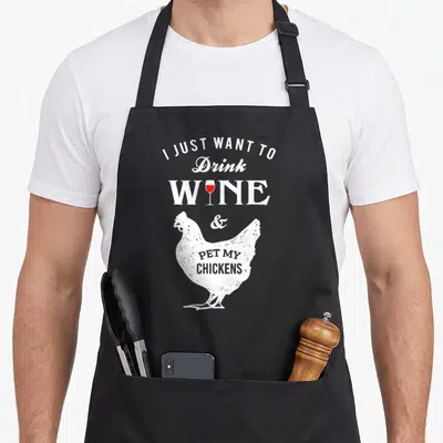 Drink chicken apron - Distressed white chicken with red wine glass and stacked text reading I just want to drink wine — shown on a black cotton canvas apron against a white background
