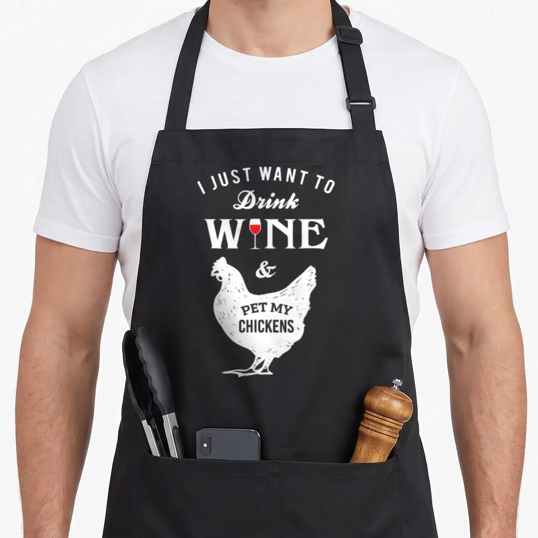 Drink chicken apron - Distressed white chicken with red wine glass and stacked text reading I just want to drink wine — shown on a black cotton canvas apron against a white background