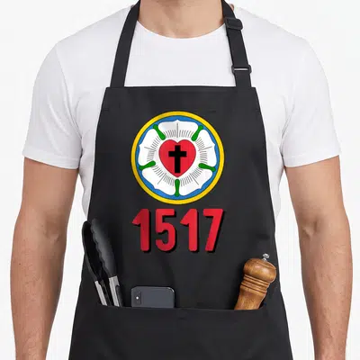 Lutheran protestant rose apron - Circular Luther Rose emblem with red heart black cross and 1517 text — shown on a black cotton canvas apron against a white background
