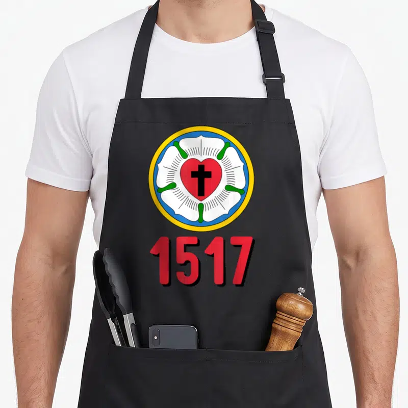 Lutheran protestant rose apron - Circular Luther Rose emblem with red heart black cross and 1517 text — shown on a black cotton canvas apron against a white background