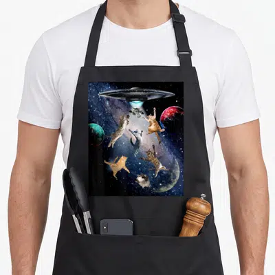 Ufo galaxy cat apron - Silver UFO beams light on six floating cats among three planets in space — shown on a black cotton canvas apron against a white background