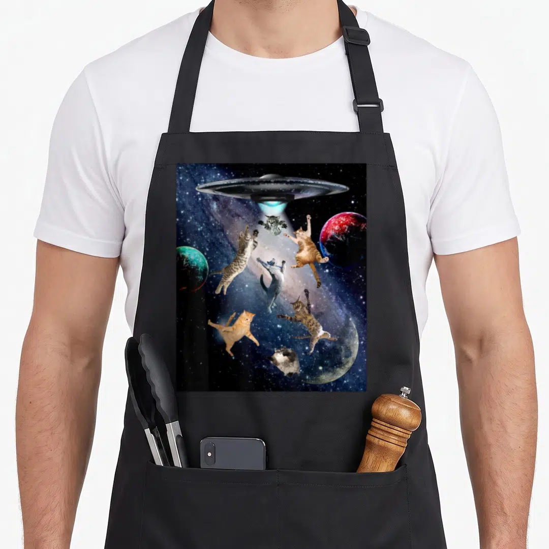 Ufo galaxy cat apron - Silver UFO beams light on six floating cats among three planets in space — shown on a black cotton canvas apron against a white background
