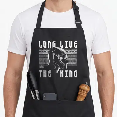 Live urban apron - Distressed Black Panther head over tribal pattern with Long Live The King text — shown on a black cotton canvas apron against a white background