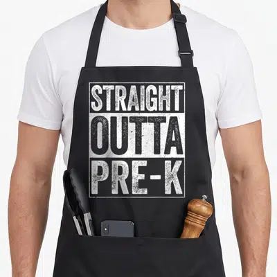 Graduation preschool apron - White and grey distressed text reading STRAIGHT OUTTA PRE-K inside a rectangular border — shown on a black cotton canvas apron against a white background