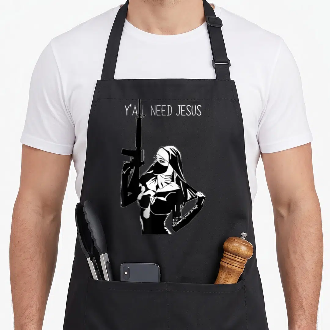 Nun machine apron - White Y'all Need Jesus text above black and white line art of a masked nun holding a rifle — shown on a black cotton canvas apron against a white background