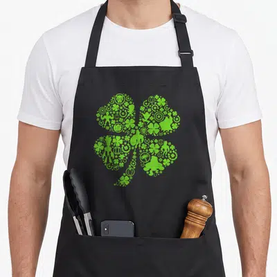 Heroe leaf st patrick day aprons - Green shamrock shape filled with superhero silhouettes and lucky icons like — shown on a black cotton canvas apron against a white background