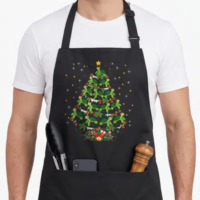 Sea christmas tree apron - Cartoon green sea turtles arranged in a Christmas tree shape with a yellow star and red gift — shown on a black cotton canvas apron against a white background