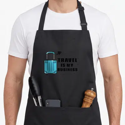 Planner travel aprons - Blue suitcase next to stacked text Travel Is My Business with dotted flight path — shown on a black cotton canvas apron against a white background