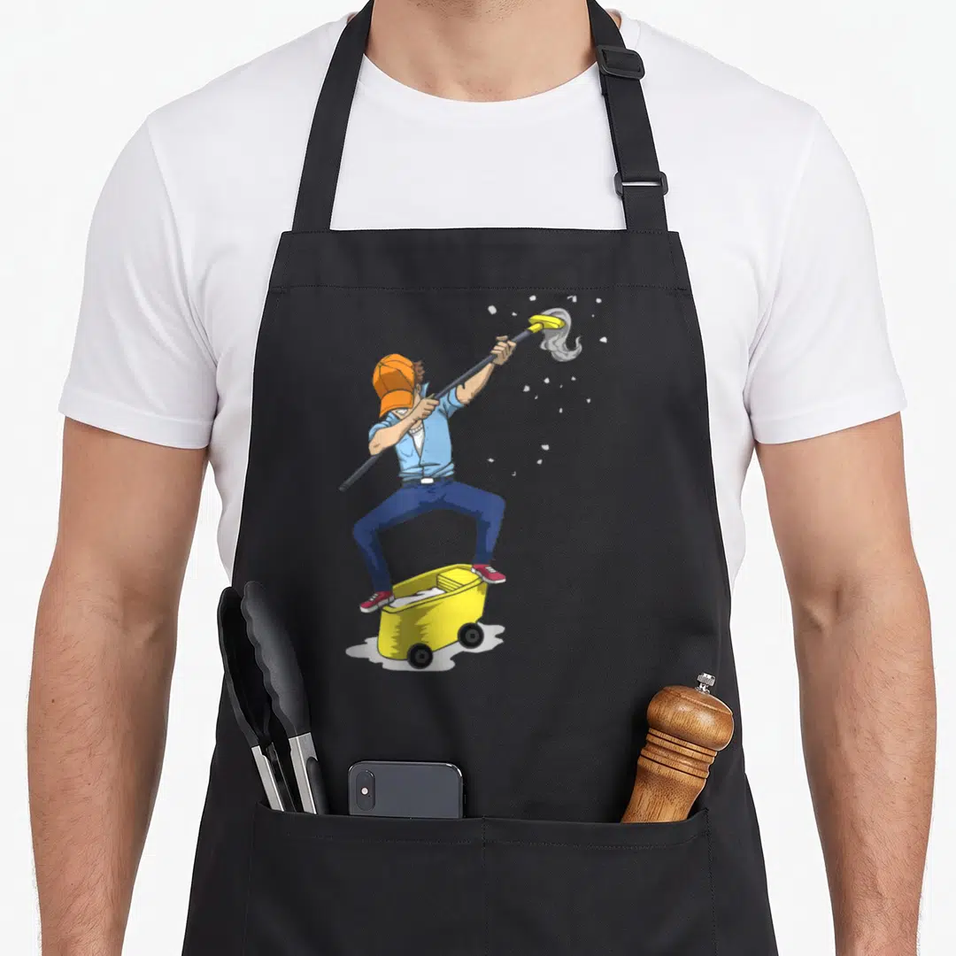 Dabbing janitor apron - Cartoon man in blue shirt and orange hat dabbing on yellow mop bucket holding mop aloft — shown on a black cotton canvas apron against a white background