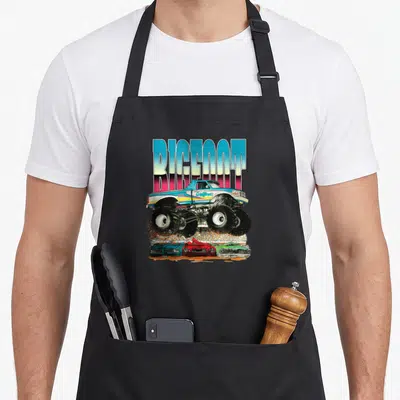 Wildfoot car apron - Retro monster truck crushing three cars under BIGFOOT text in blue pink red green — shown on a black cotton canvas apron against a white background