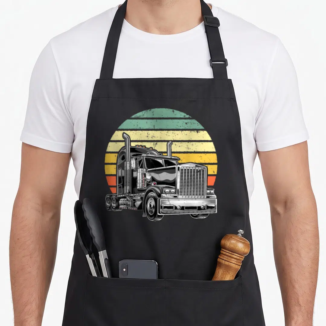 Trailer semi truck apron - Black semi-truck illustration against a retro striped sun in green, yellow, and orange colors — shown on a black cotton canvas apron against a white background