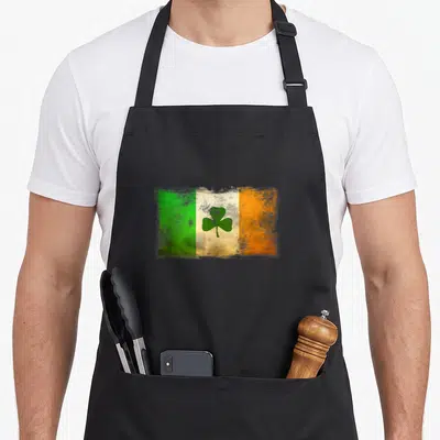 Distressed ireland apron - Distressed Irish flag with green white orange stripes and centered shamrock — shown on a black cotton canvas apron against a white background