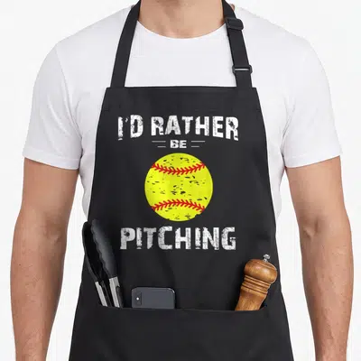Rather pitcher apron - I'D RATHER BE PITCHING text surrounding a yellow softball with red stitching — shown on a black cotton canvas apron against a white background