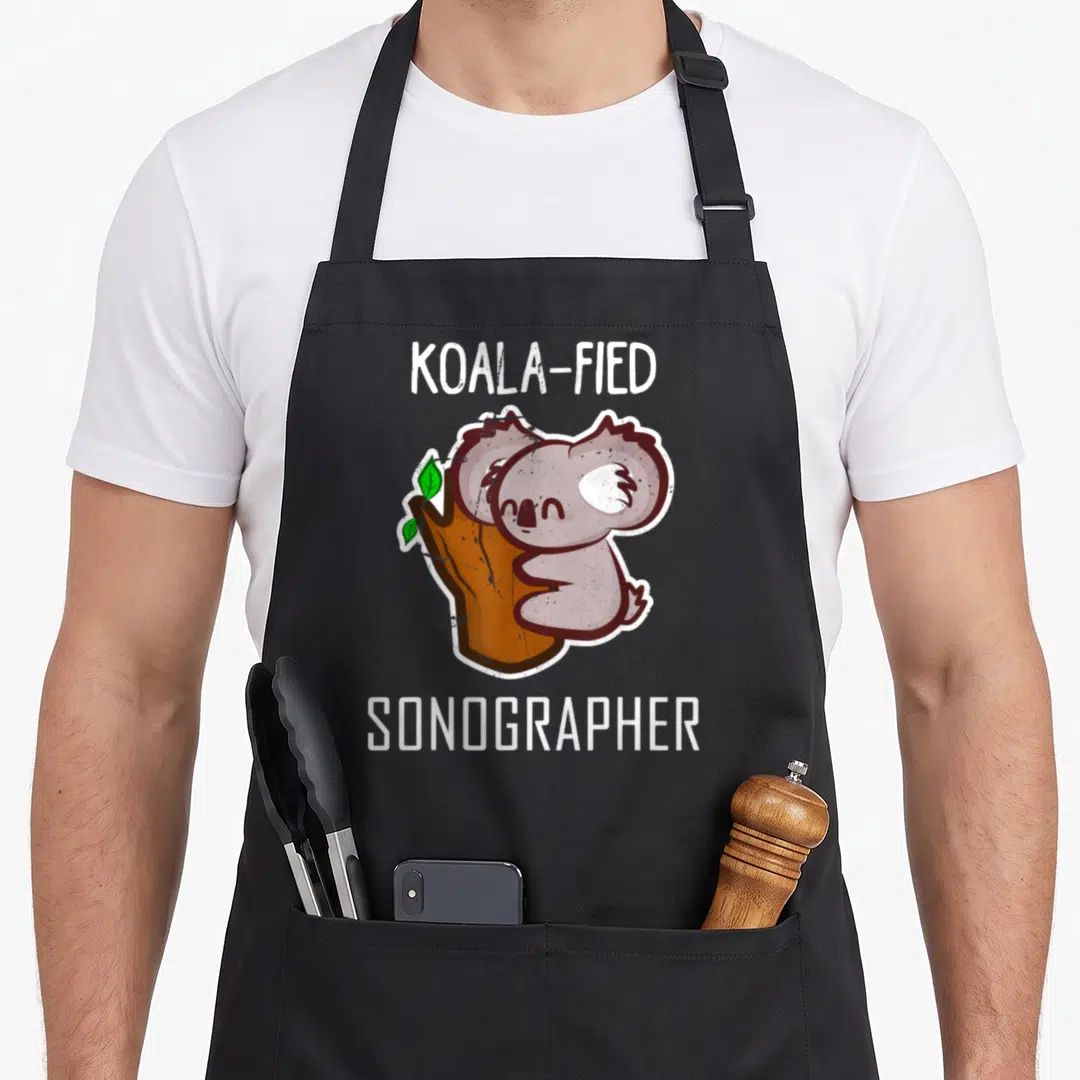 Koal sonographer apron - Cartoon koala hugging tree with text KOALA-FIED SONOGRAPHER — shown on a black cotton canvas apron against a white background