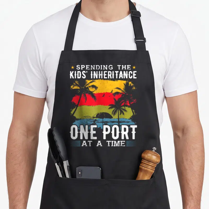 Cruise port orange apron - Retro tropical sunset with palm trees and text spending the kids inheritance one port — shown on a black cotton canvas apron against a white background