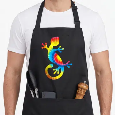 Gecko tie-dye apron - Rainbow tie-dye gecko silhouette in red yellow green blue — shown on a black cotton canvas apron against a white background