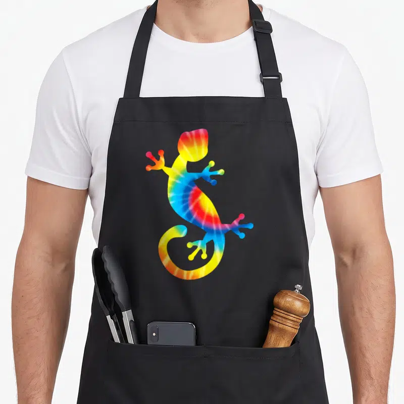 Gecko tie-dye apron - Rainbow tie-dye gecko silhouette in red yellow green blue — shown on a black cotton canvas apron against a white background