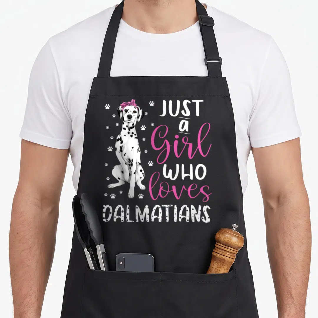 Funny dalmatian dog apron - Cartoon dalmatian with pink bow and white paw prints next to stacked text reading Just — shown on a black cotton canvas apron against a white background