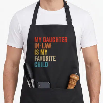 Law family mom and daughter aprons - Stacked colorful text reading My Daughter In-Law Is My Favorite Child in red — shown on a black cotton canvas apron against a white background