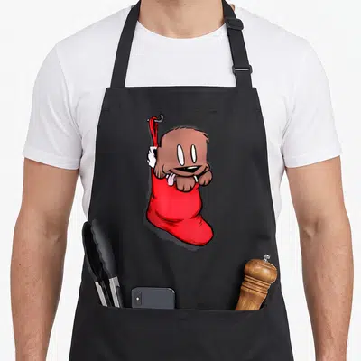 Puppy womens christmas aprons - Cartoon brown dog with pink tongue inside red Christmas stocking hanging from grey hook — shown on a black cotton canvas apron against a white background