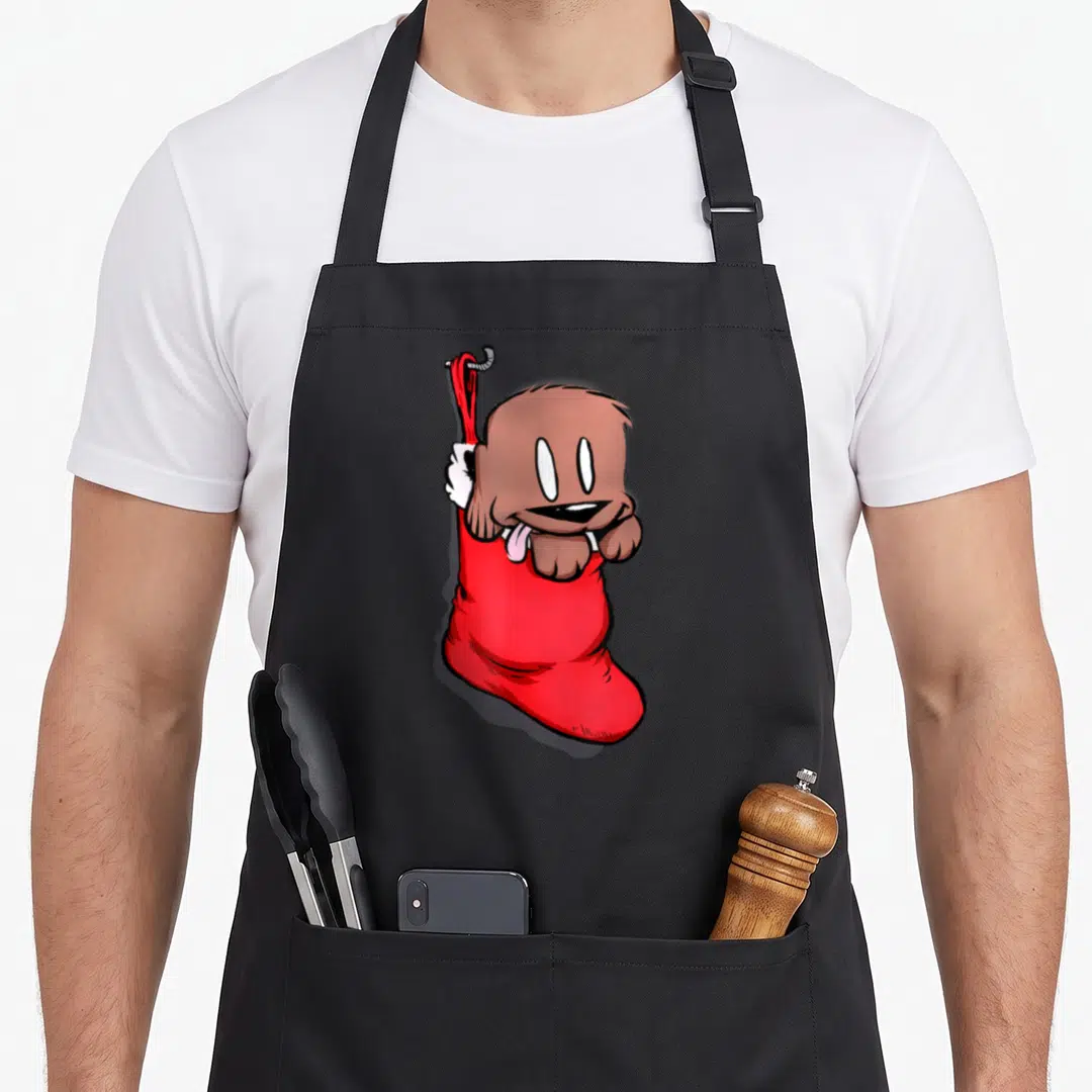Puppy womens christmas aprons - Cartoon brown dog with pink tongue inside red Christmas stocking hanging from grey hook — shown on a black cotton canvas apron against a white background