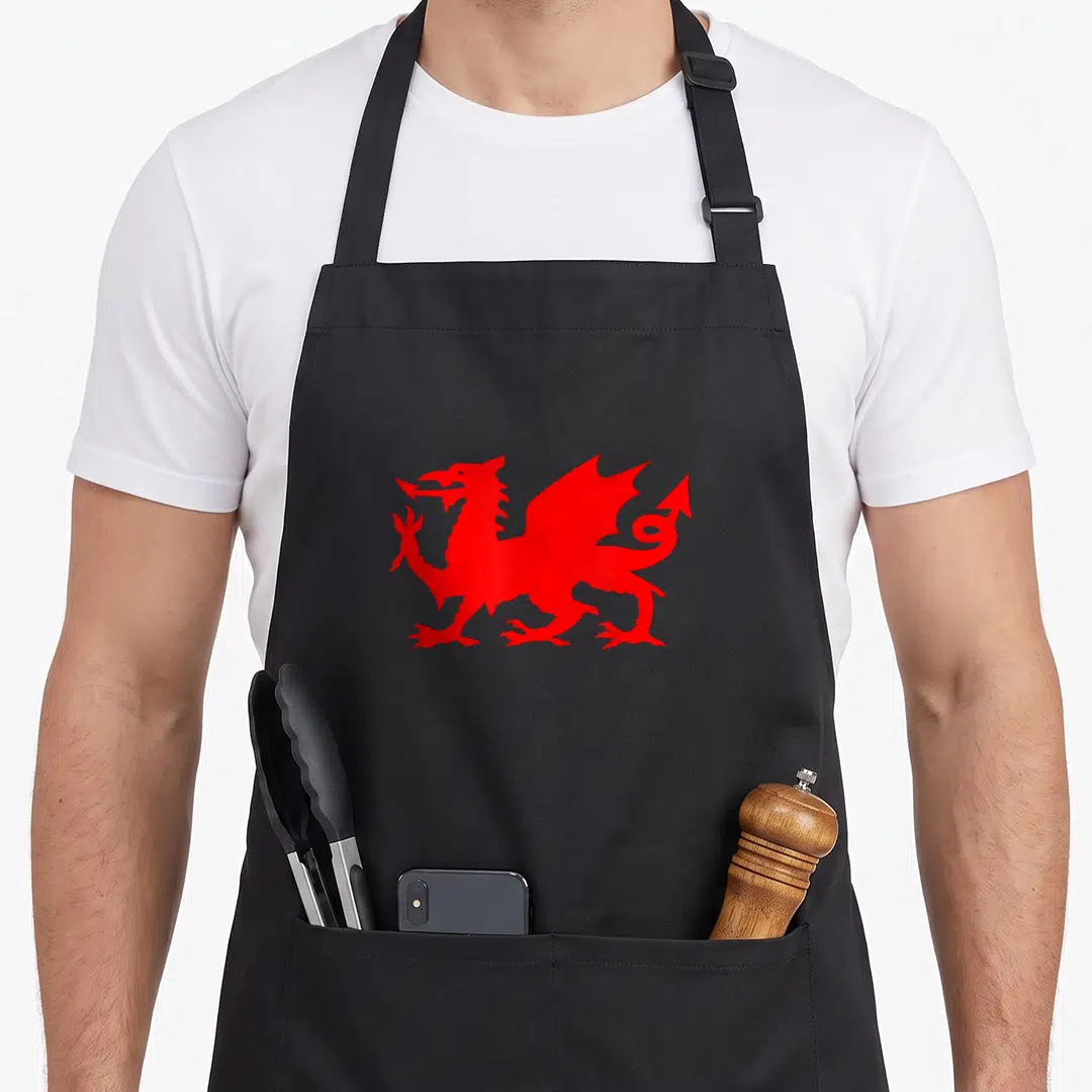 Wale dragon apron - Red Welsh dragon facing left with wings spread and forked tail — shown on a black cotton canvas apron against a white background