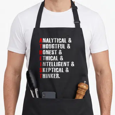 Atheist religion science apron - Stacked white words with red first letters spelling ATHEIST vertically on black — shown on a black cotton canvas apron against a white background