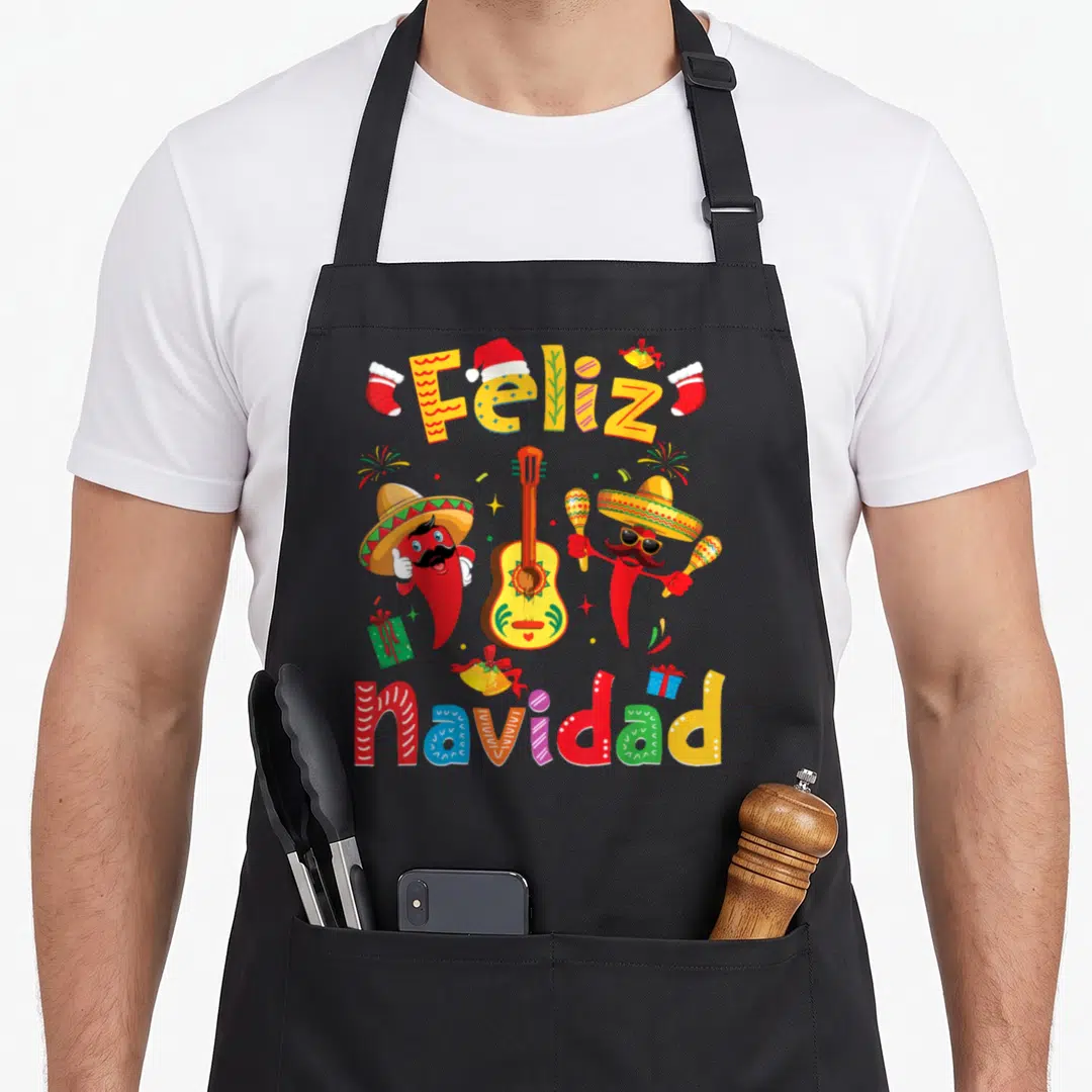Navidad xmas apron - Two chili peppers in sombreros flank a guitar under Feliz navidad text in red yellow green blue — shown on a black cotton canvas apron against a white background