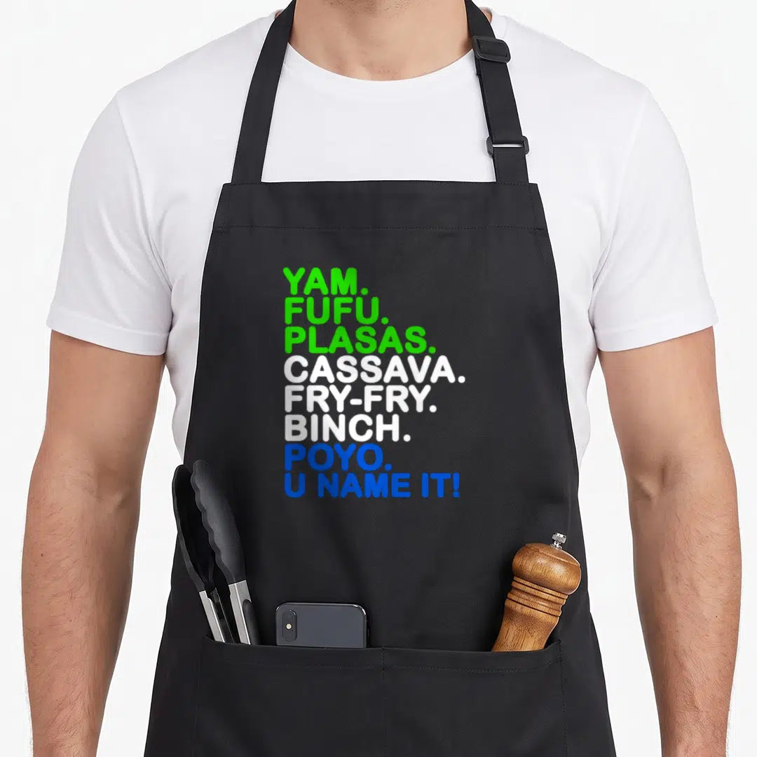 Sierra food aprons - Stacked text listing yam, fufu, cassava, fry-fry, binch, poyo, u name it in green white blue — shown on a black cotton canvas apron against a white background