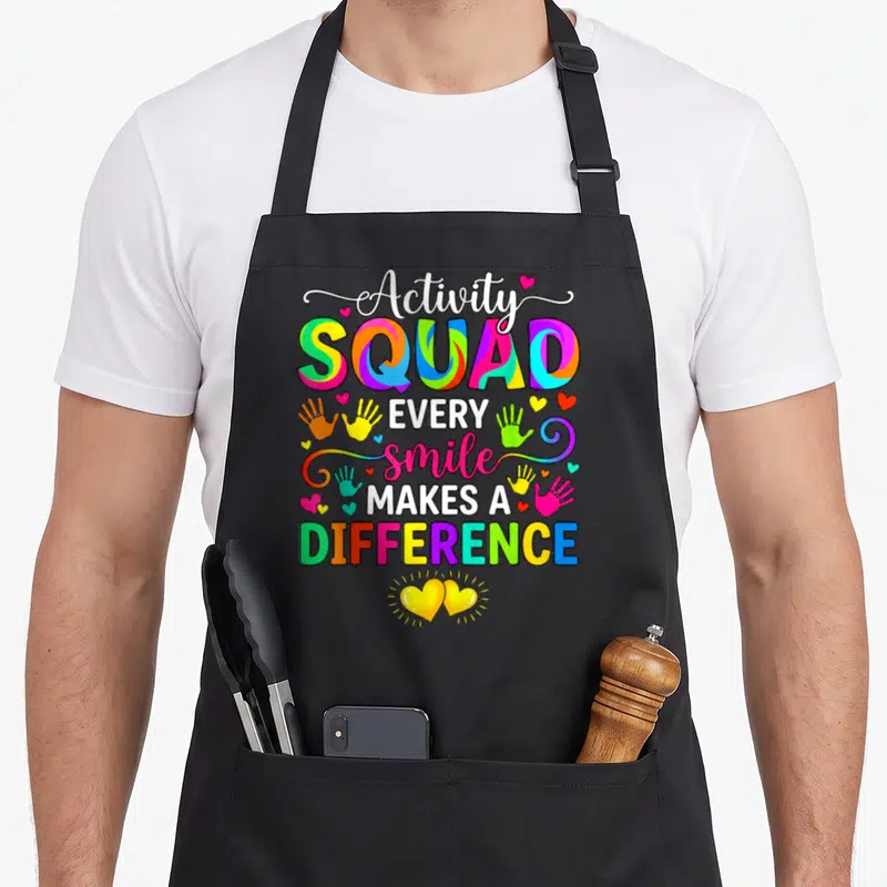 Professional week activity apron - Stacked text Activity SQUAD EVERY smile MAKES A DIFFERENCE with colorful handprints — shown on a black cotton canvas apron against a white background