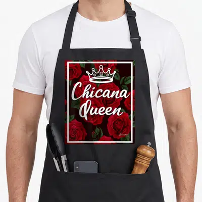Chicana rose apron - White crown and script over red roses enclosed in a white border — shown on a black cotton canvas apron against a white background