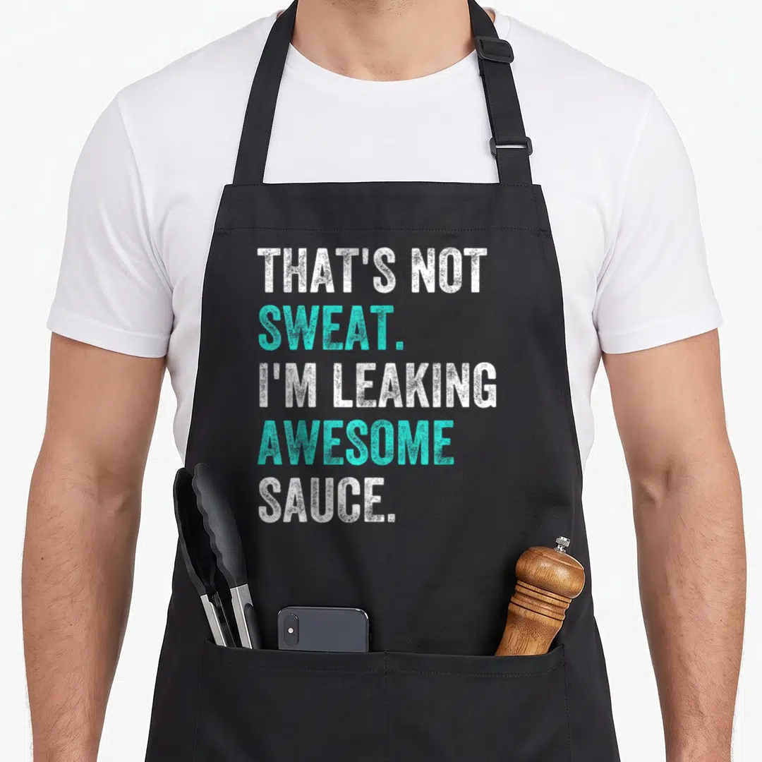 Sweat sauce apron - Stacked white and turquoise distressed text reading that's not sweat i'm leaking awesome sauce — shown on a black cotton canvas apron against a white background