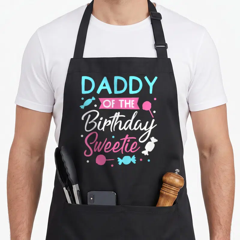 Sweetie daddy apron - DADDY OF THE Birthday Sweetie text with cyan and pink candies and lollipops — shown on a black cotton canvas apron against a white background