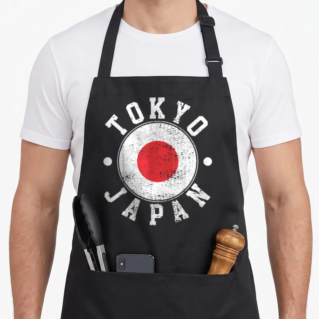 Funny tokyo japan apron - Distressed Japanese flag with TOKYO JAPAN text and two white dots — shown on a black cotton canvas apron against a white background