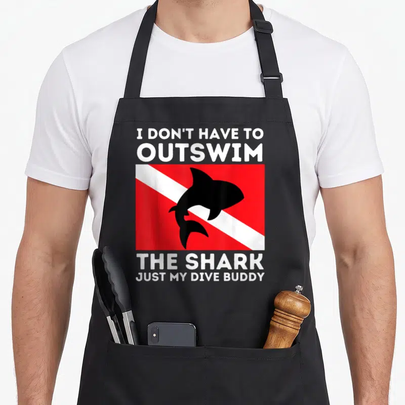 Outswim buddy aprons - I DON'T HAVE TO OUTSWIM THE SHARK text with black shark on red and white flag — shown on a black cotton canvas apron against a white background