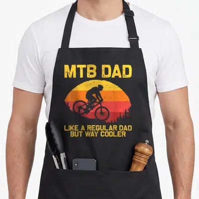 Father bicycle apron - Retro sunset with grey mountain biker silhouette and yellow MTB DAD text on black fabric — shown on a black cotton canvas apron against a white background