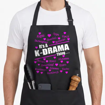 Funny drama korean apron - White K-Drama slogan between pink lines surrounded by pink Korean words and hearts — shown on a black cotton canvas apron against a white background